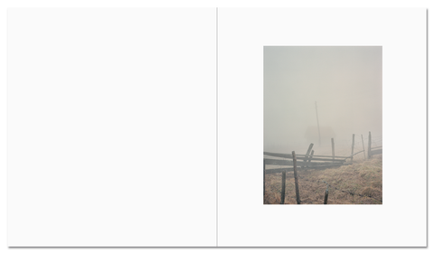 Photograph from the Mountain Black Heart photography book by MACK, showcasing a engulfing fog annd a fence that has fallen with barbed wire