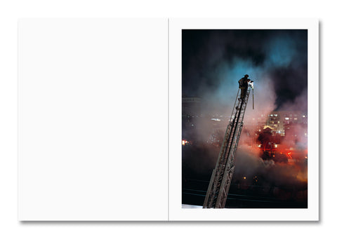 Firefighter on a ladder amidst smoke and flames at night.