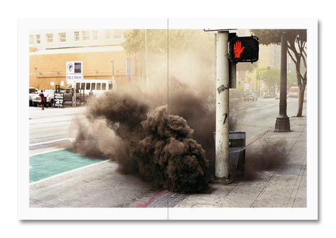 Smoke on a city street, featuring a red hand traffic signal.