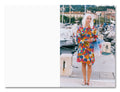 Woman in a colorful floral dress standing on a dock with boats and buildings in the background
