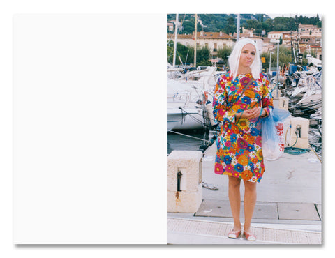Woman in a colorful floral dress standing on a dock with boats and buildings in the background